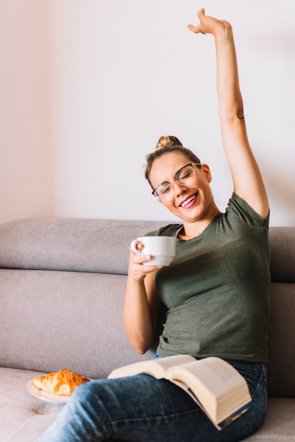 happy relaxed young woman with book lap stretching her hand holding coffee cup